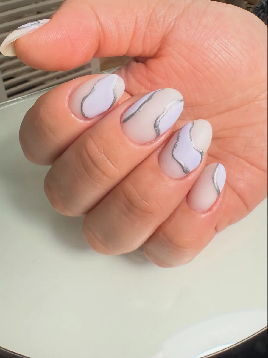 Manicura clara con líneas onduladas plateadas realizada por María Suárez